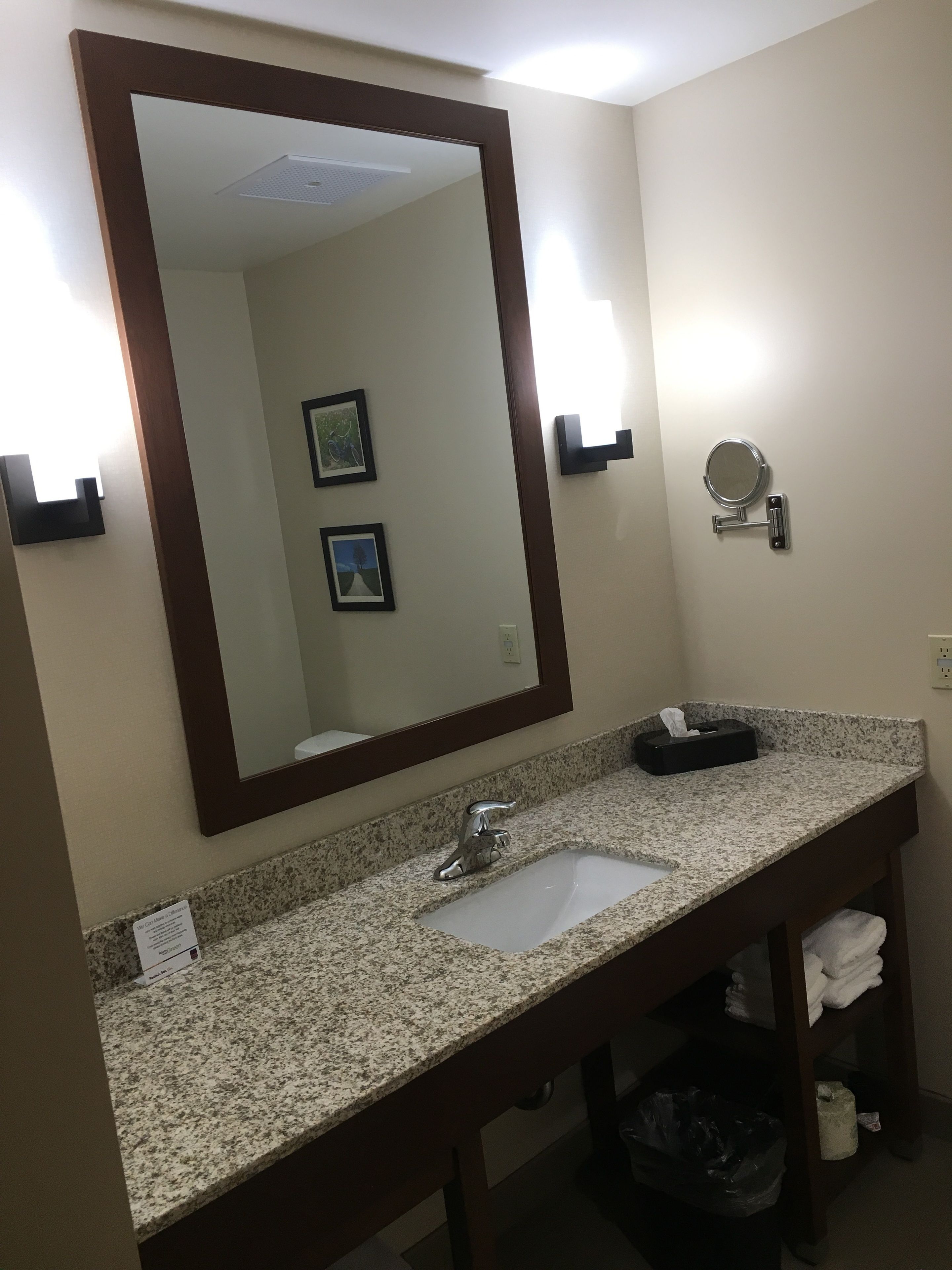 A bathroom with a granite countertop sink, a large mirror, and a small round mirror on the wall.