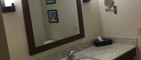 A bathroom with a granite countertop sink, a large mirror, and a small round mirror on the wall.