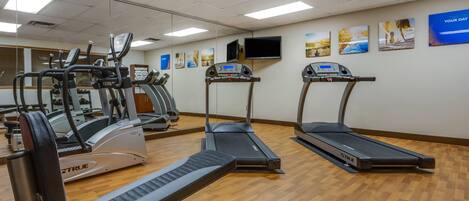 Un gimnasio con cintas de correr, elípticas y una banca.