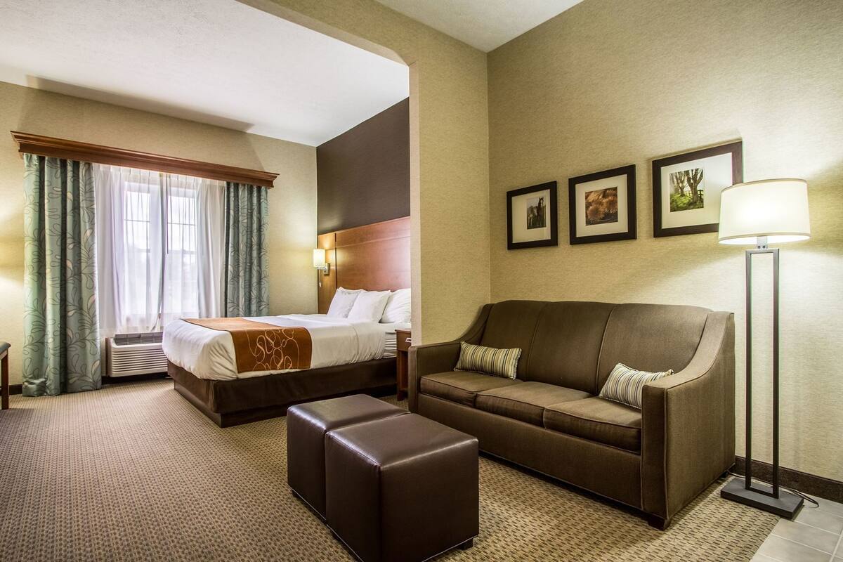 A hotel room with a bed, a sofa, a coffee table, a lamp, and framed pictures on the wall.