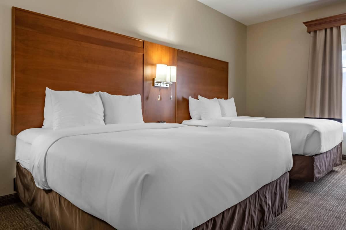 A hotel room with two beds, a wooden headboard, a wall-mounted light, and a window with curtains.