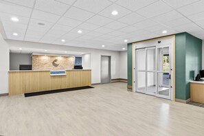 A reception area with a wooden reception desk, a stone accent wall, a glass door entrance, and a tiled ceiling. - Comfort Suites Hotel and Conference Center (Berlin)