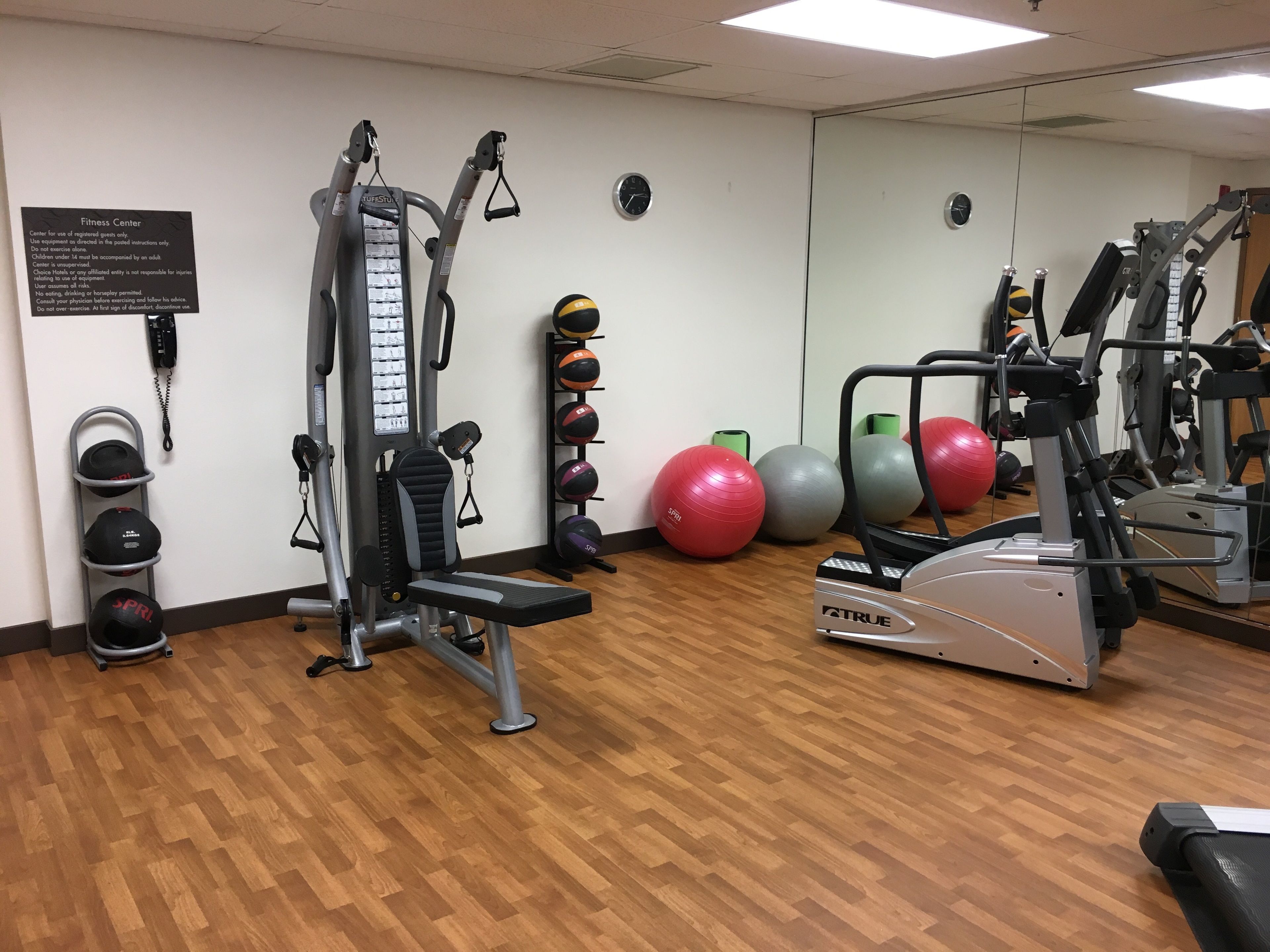 A fitness center with exercise equipment, a wall-mounted phone, and a rack of sports balls.