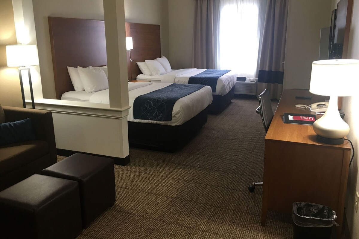 Ein Hotelzimmer mit zwei Betten, einem Schreibtisch, einem Stuhl, einer Lampe und einem Mülleimer.