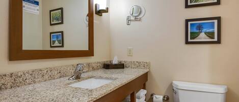 A bathroom with a granite countertop sink, a mirror, a toilet, and framed pictures on the wall.