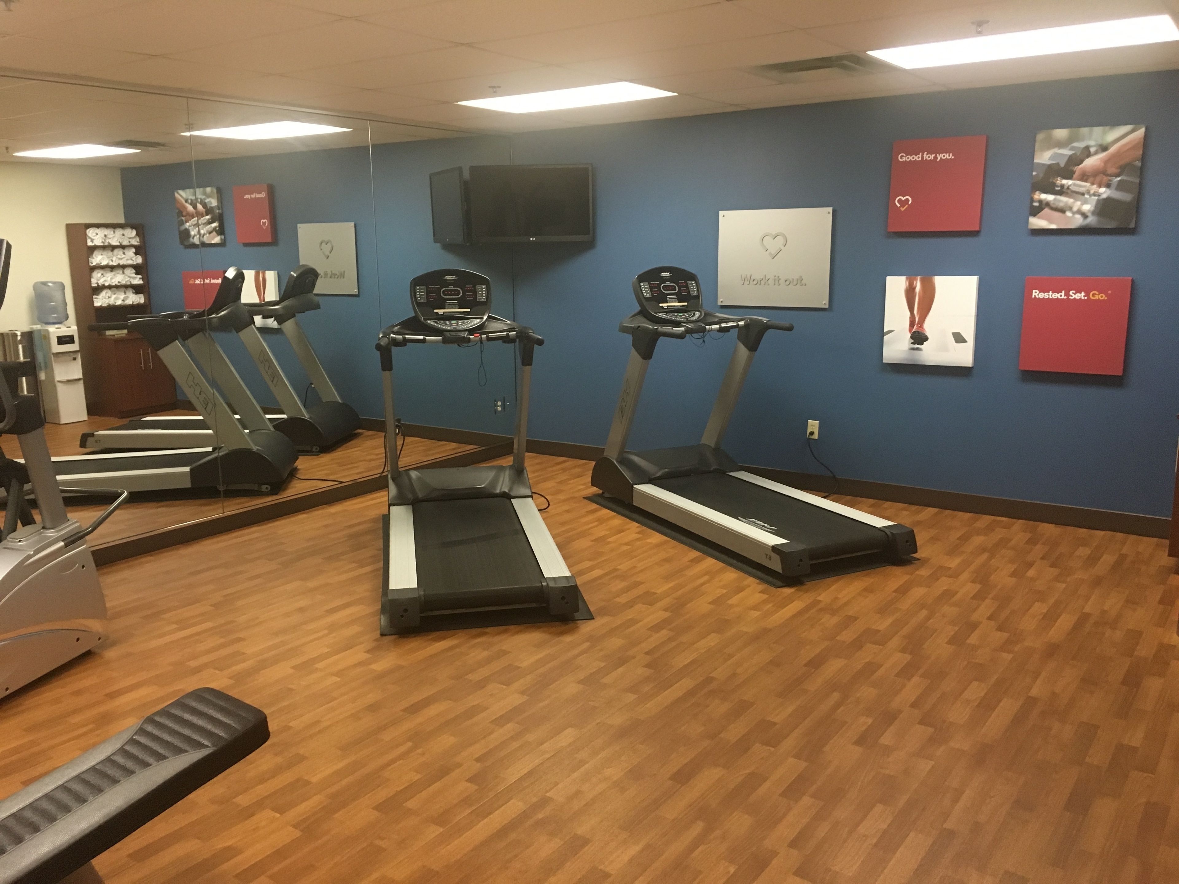 A gym with treadmills, a water cooler, and motivational posters on the wall.