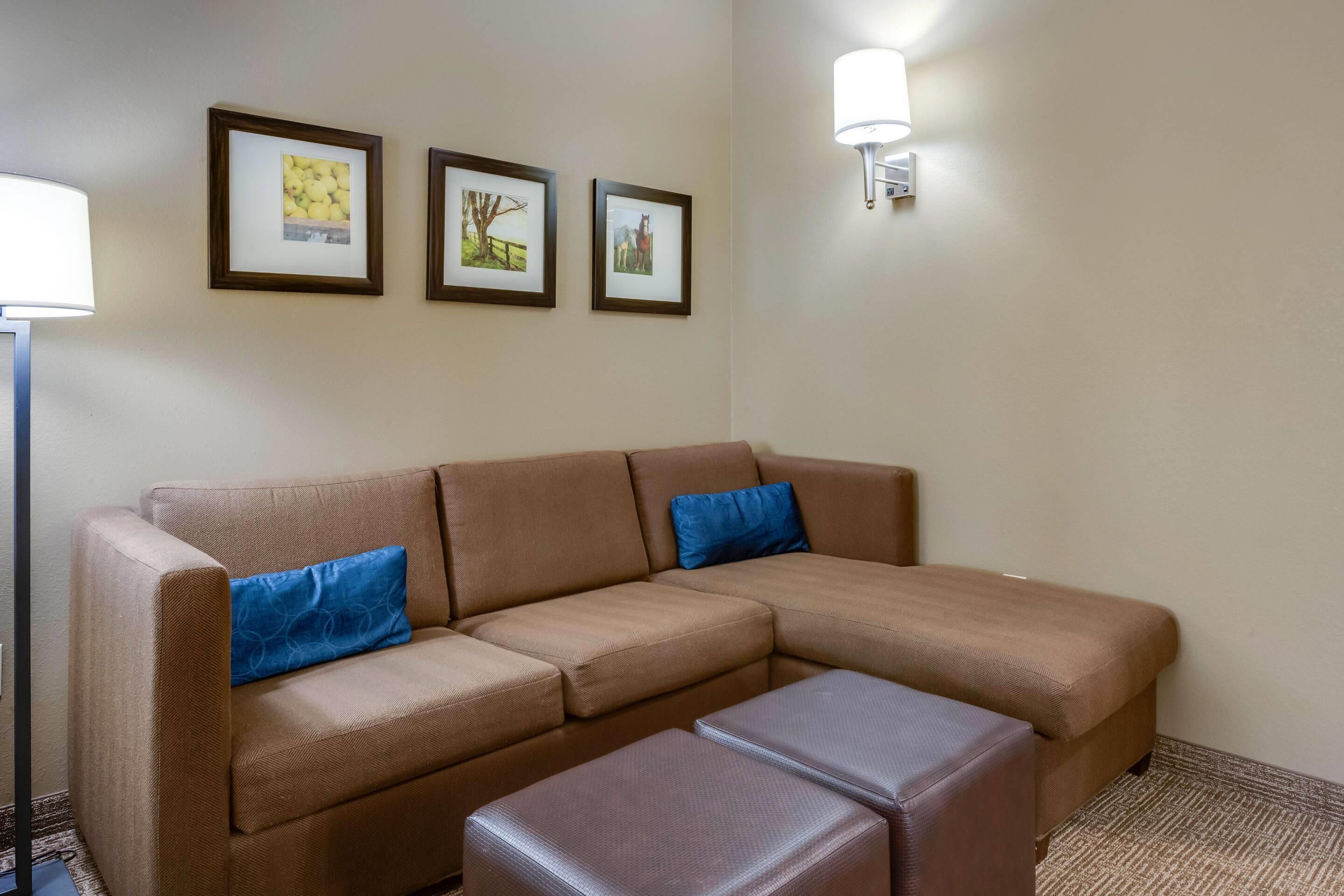 A brown sofa with two blue pillows, a brown ottoman, and three framed pictures on the wall.