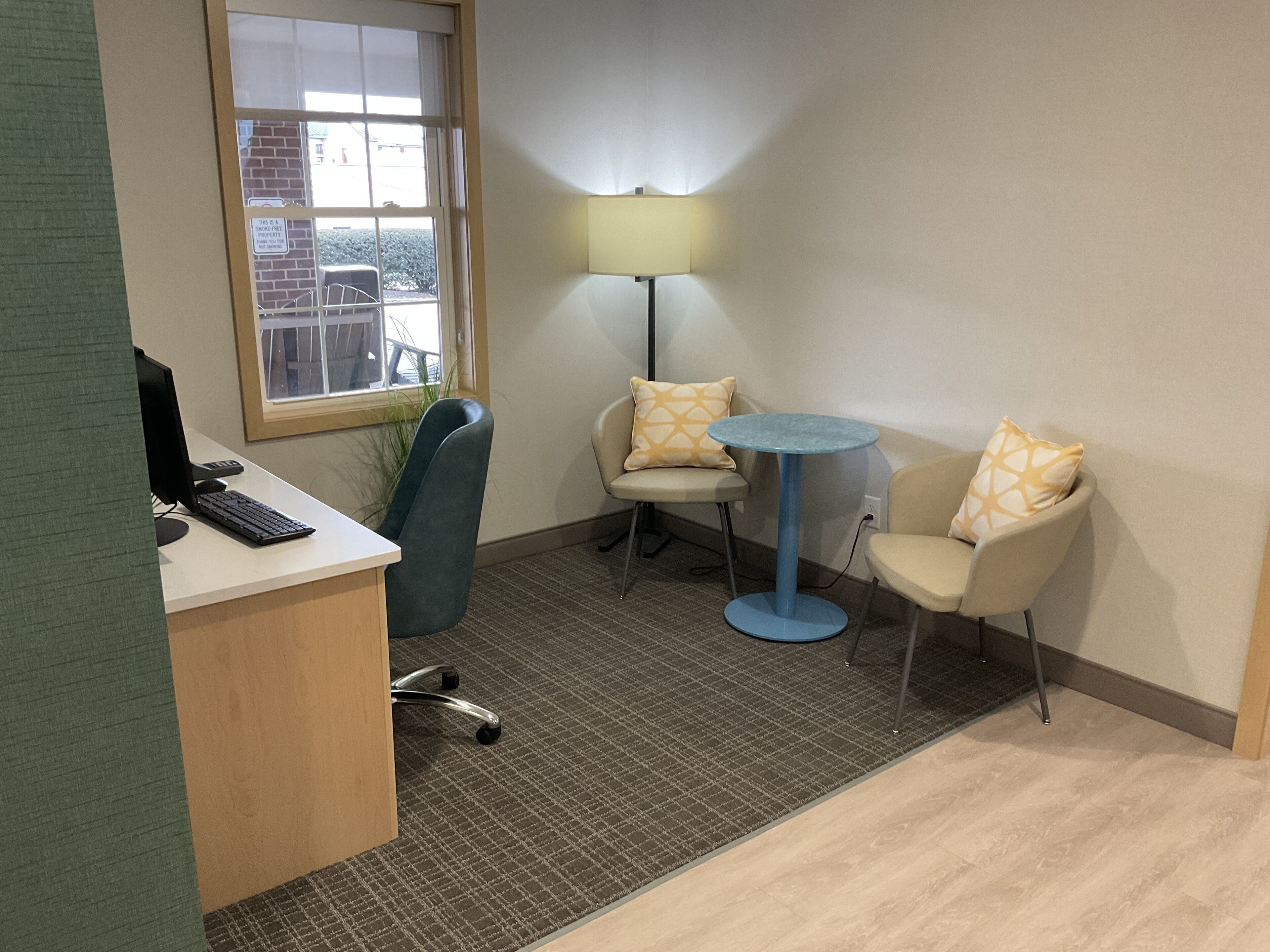 A small office with a desk, computer, and two chairs. There is a window with a view of the outside.