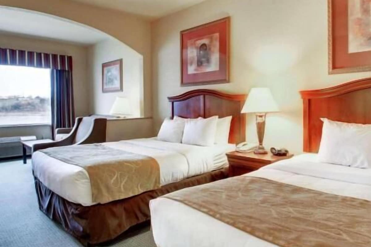 A hotel room with two beds, a desk, a chair, and a window with curtains.