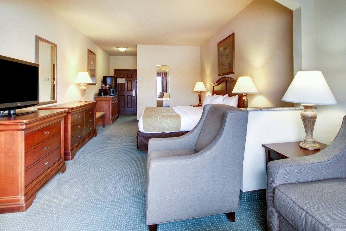 A hotel room with a bed, two armchairs, a desk with a television, and a dresser.