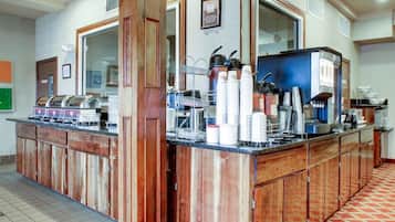A buffet counter with a variety of food items, a coffee station, and a seating area with a patterned floor.