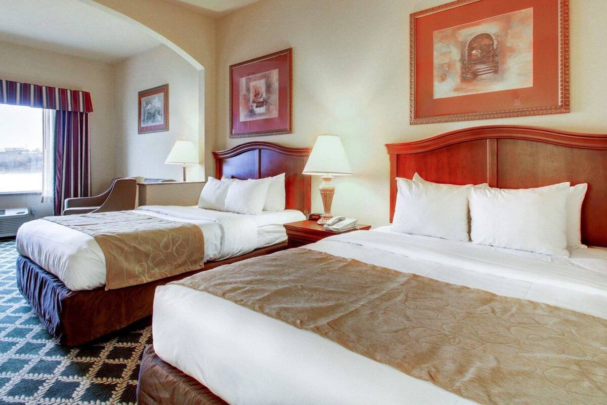 A hotel room with two beds, a desk, a chair, and a window with curtains.