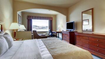 Een hotelkamer met een groot bed, een bureau met stoel, een televisie, een dressoir en een raam met gordijnen.