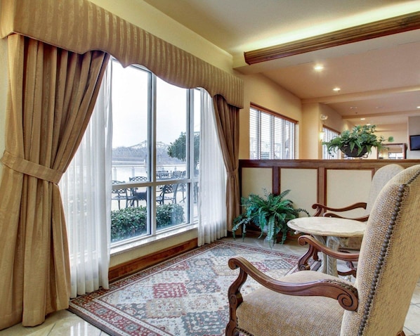 Una habitación con un ventanal grande, una alfombra estampada y una silla de madera.