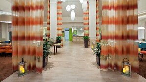 A hotel lobby with a central reception desk, potted plants, and a chandelier.