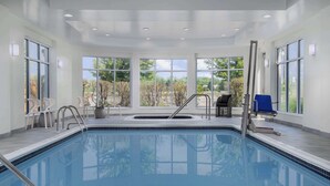 A swimming pool with clear glass walls, a hot tub, and a few lounge chairs.