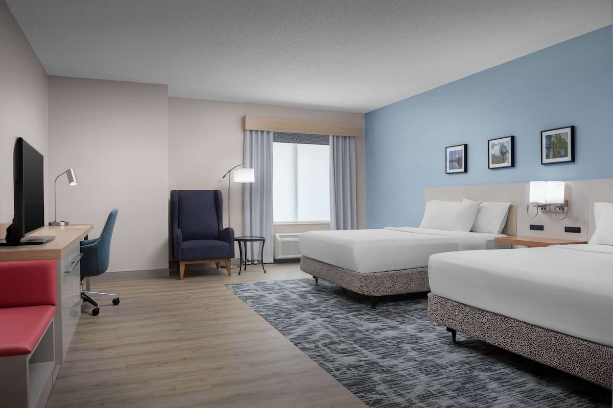 A hotel room with two beds, a desk with a computer, a chair, and a TV.