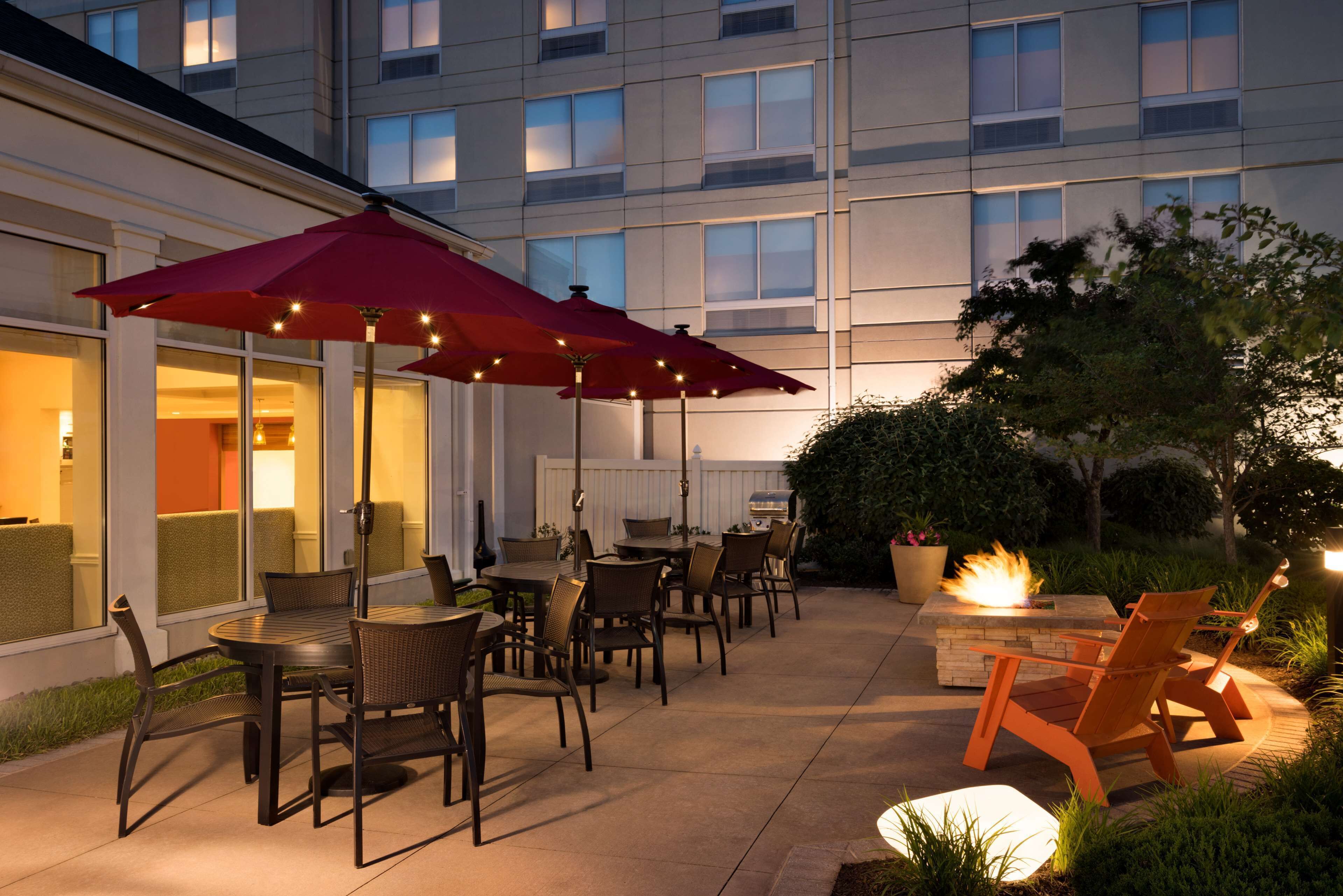 An outdoor patio area with tables and chairs, a fire pit, and umbrellas providing shade.