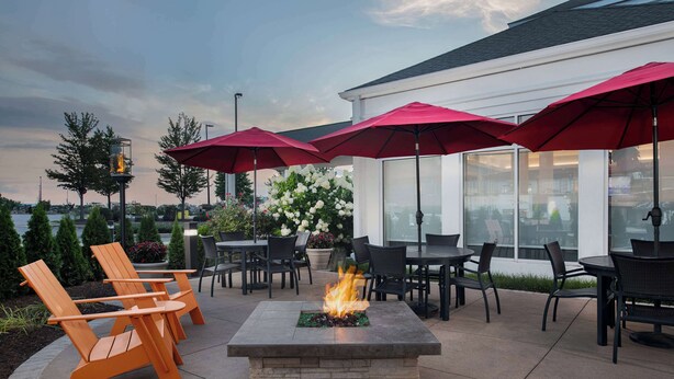 An outdoor patio with a stone fire table, orange Adirondack chairs, and red umbrellas.
