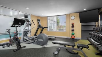 A gym with cardio machines, dumbbells, and a bench.