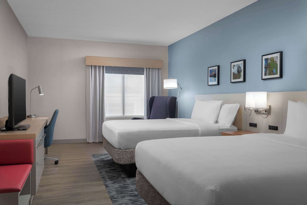 A hotel room with two beds, a desk with a computer, a chair, and a TV.