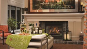 A modern living room with a fireplace, a dining table set with wine bottles and glasses, and a large framed artwork above the fireplace.