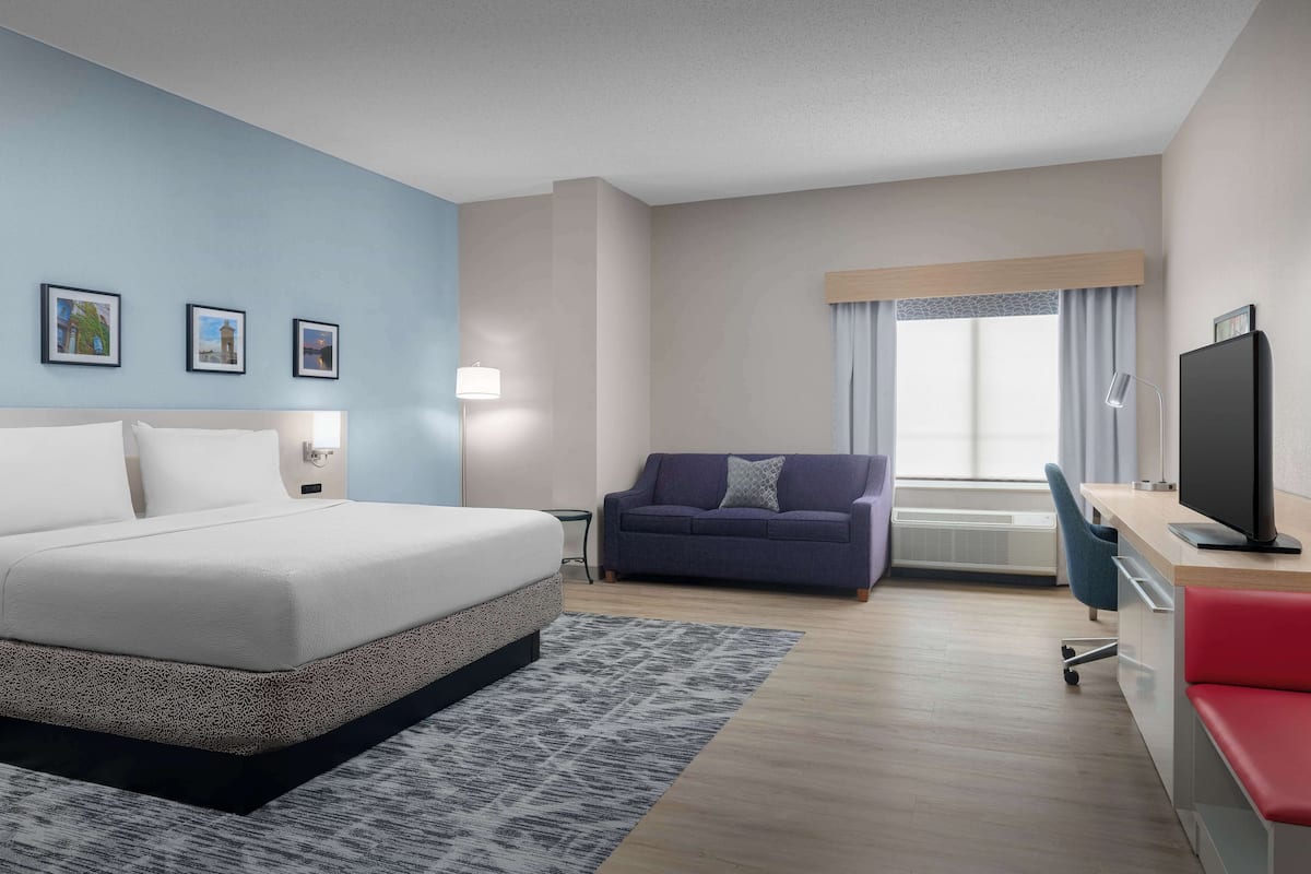 A hotel room with a bed, a desk with a computer, a sofa, and a TV.