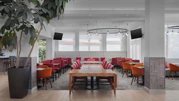 Un salón de conferencias con una gran mesa de madera, sillas rojas y una planta en maceta.