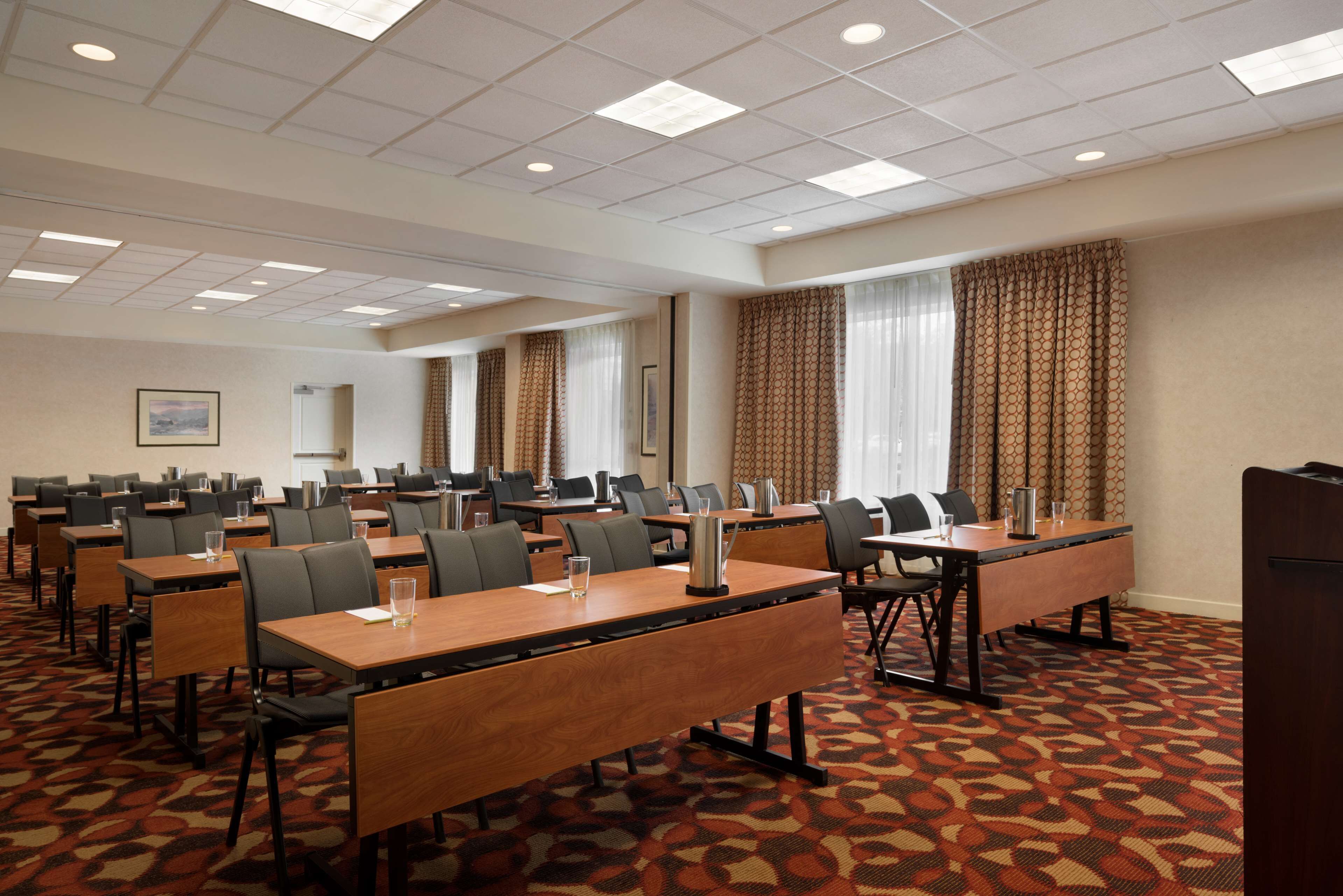 A conference room with multiple tables and chairs, arranged in rows, with a patterned carpet and a ceiling with recessed lighting.