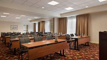 A conference room with multiple tables and chairs, arranged in rows, with a patterned carpet and a ceiling with recessed lighting.