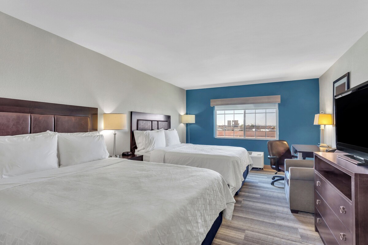 A hotel room with two beds, a desk, a chair, a TV, and a window with a view.