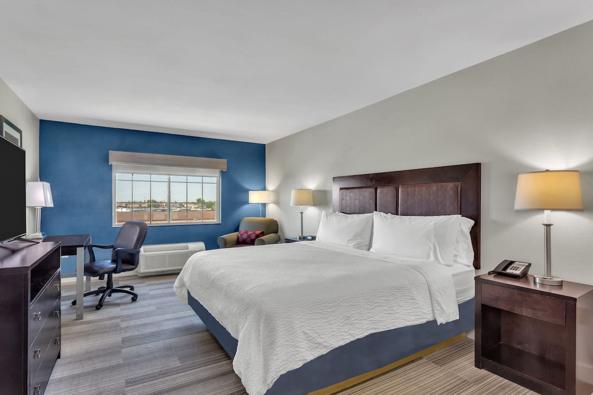A hotel room with a large bed, a desk, a chair, and a window.