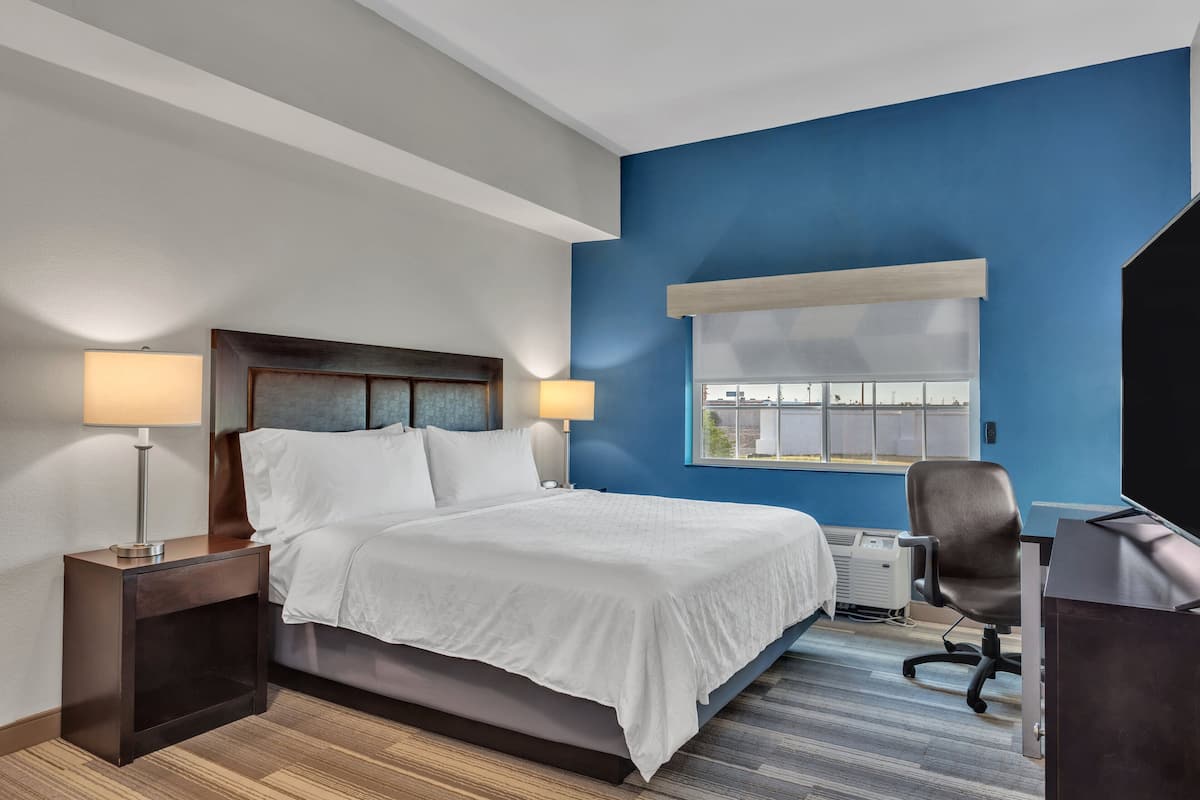 A hotel room with a bed, bedside lamps, a desk, a chair, and a window with a view.