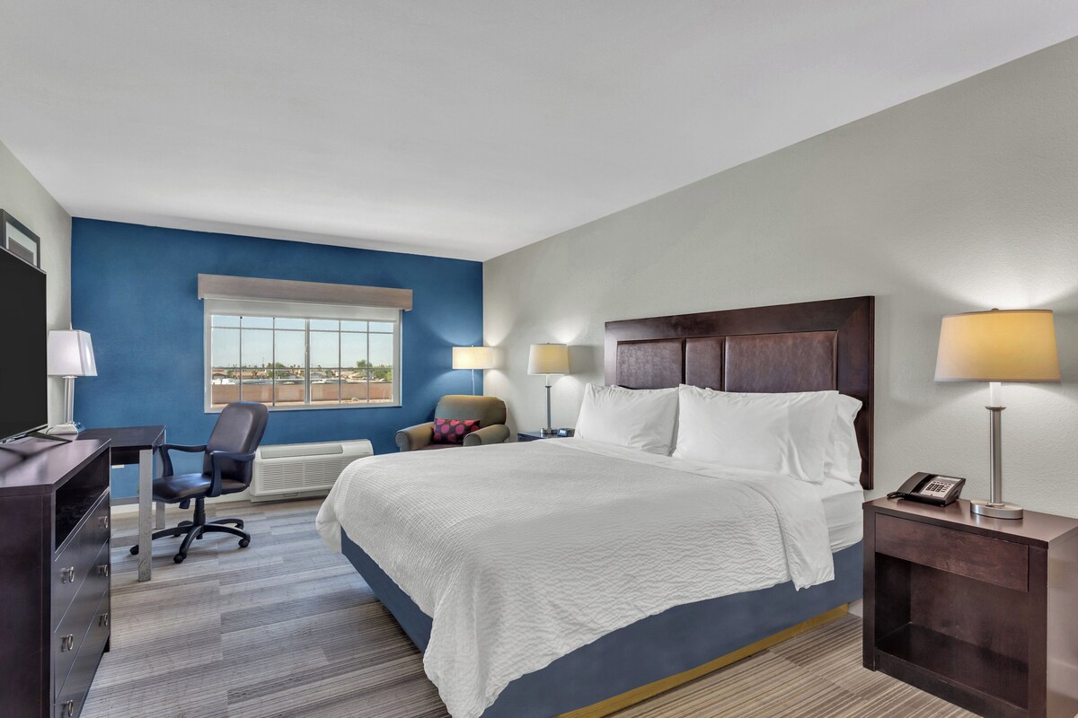 A hotel room with a large bed, a desk, a chair, and a window.