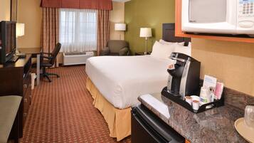 A hotel room with a bed, desk, chair, microwave, coffee maker, and a small kitchenette.