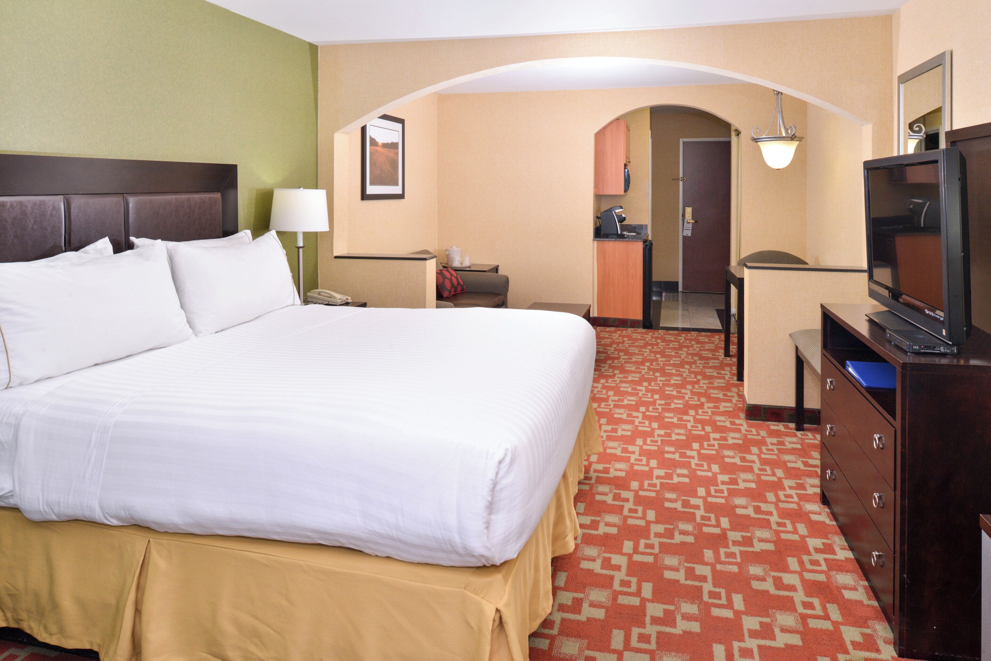 A hotel room with a large bed, a desk, a television, and a kitchenette.