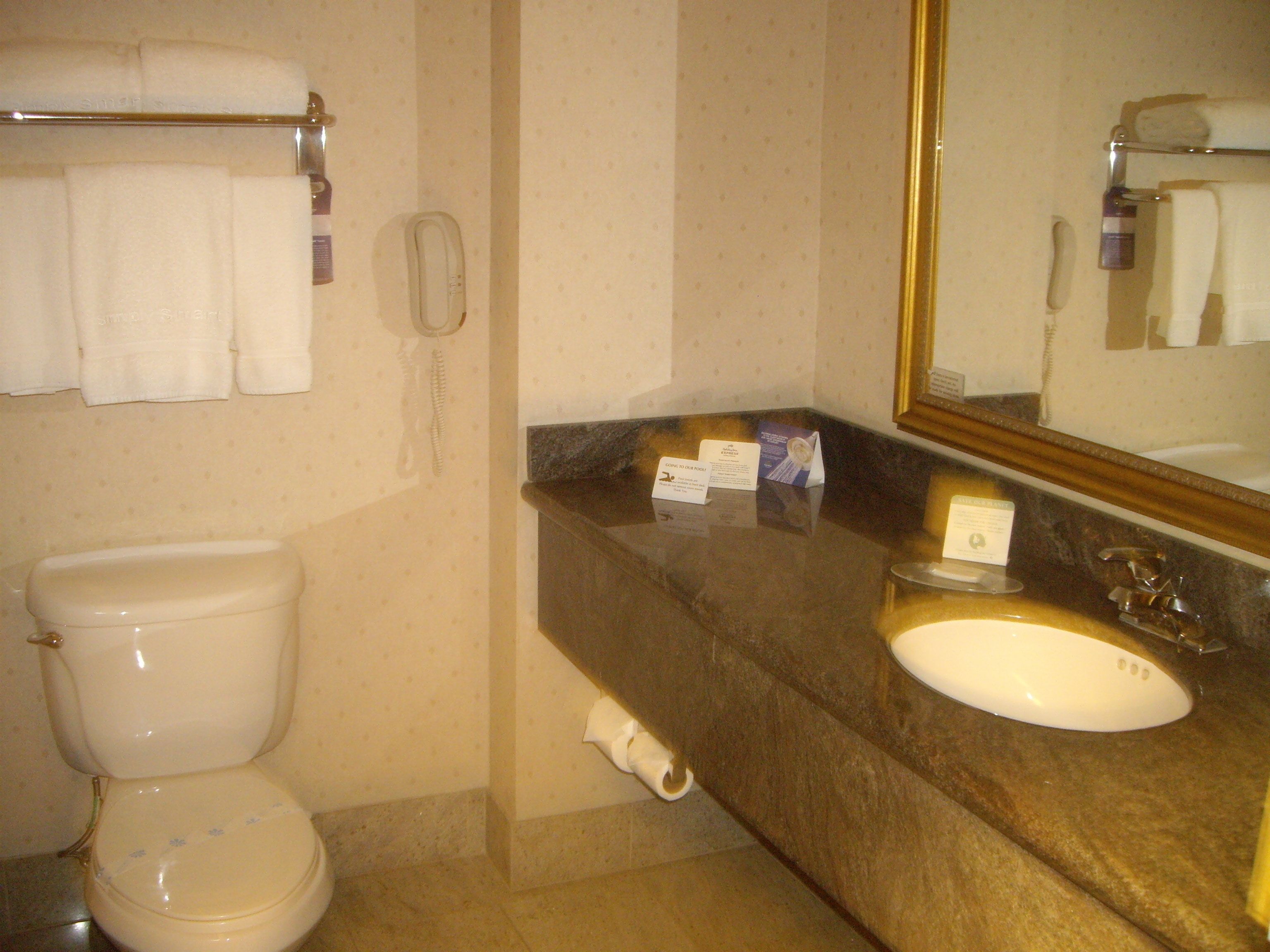 A bathroom with a toilet, sink, and mirror. There are towels hanging on a rack and a phone on the wall.
