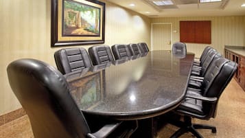 A conference room with a long table surrounded by leather chairs, a framed painting on the wall, and a door with a wooden panel.