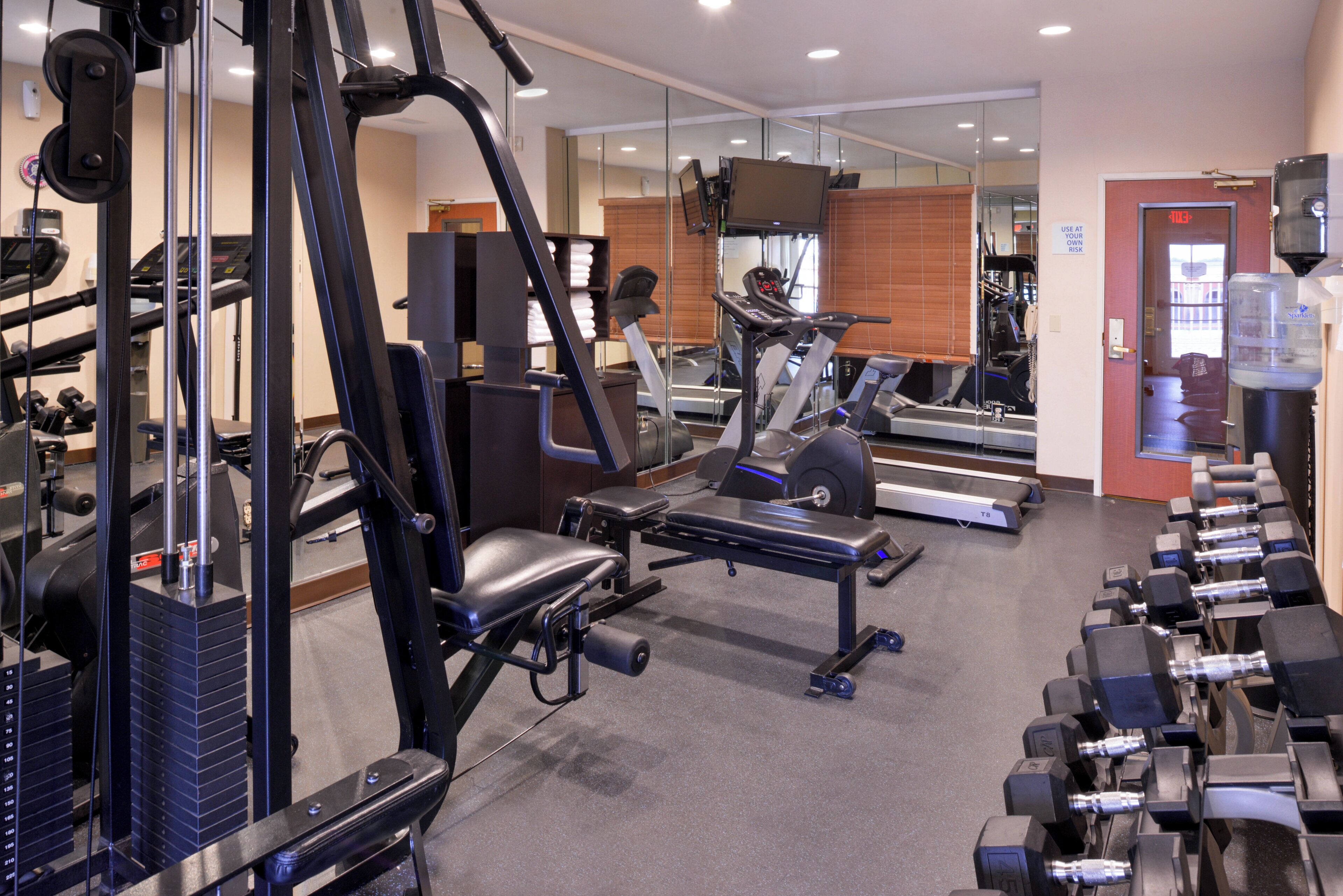 Un gimnasio con equipos de ejercicio variados, incluyendo cintas de correr, máquinas de pesas y mancuernas.