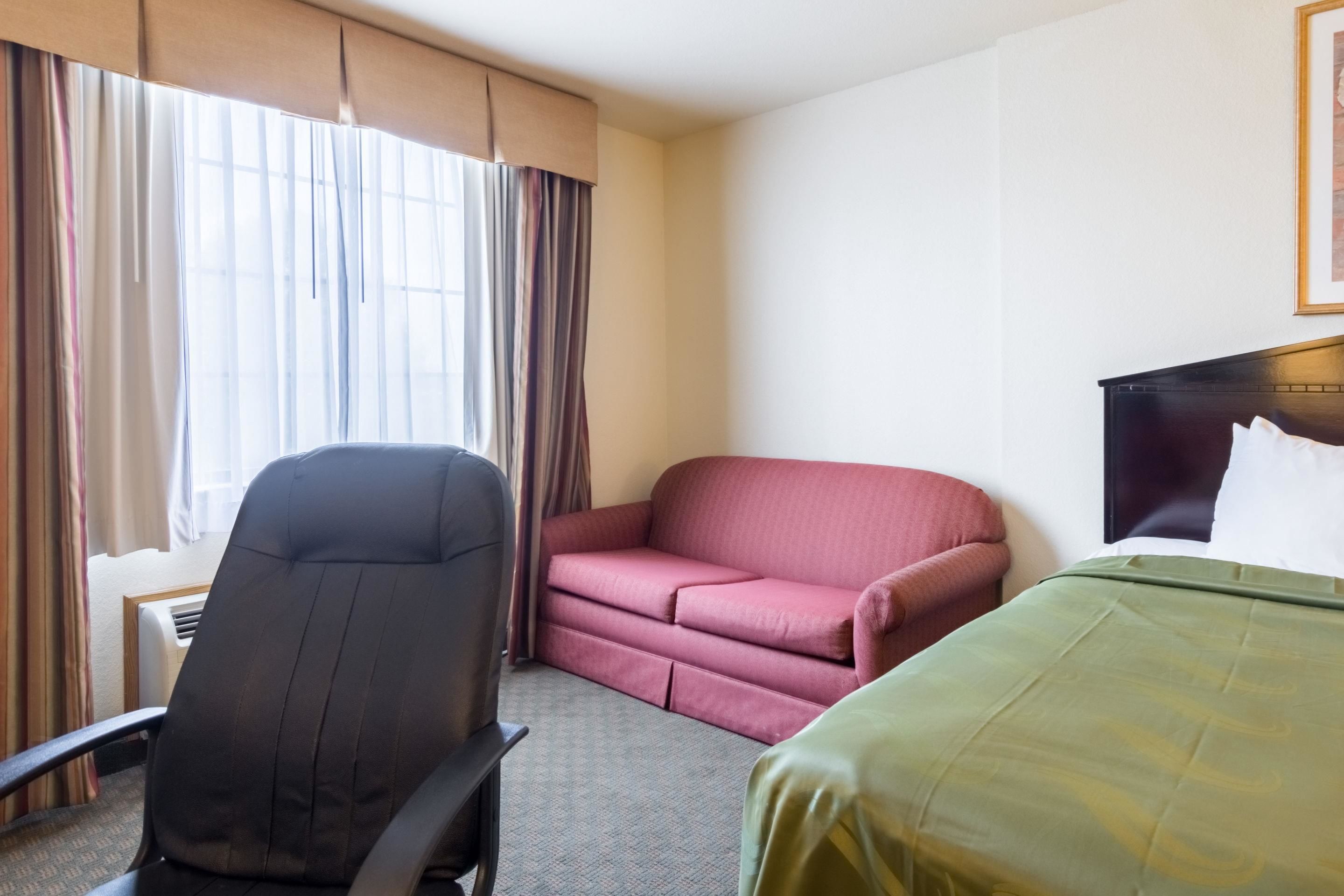 A hotel room with a bed, a desk, a chair, and a sofa.