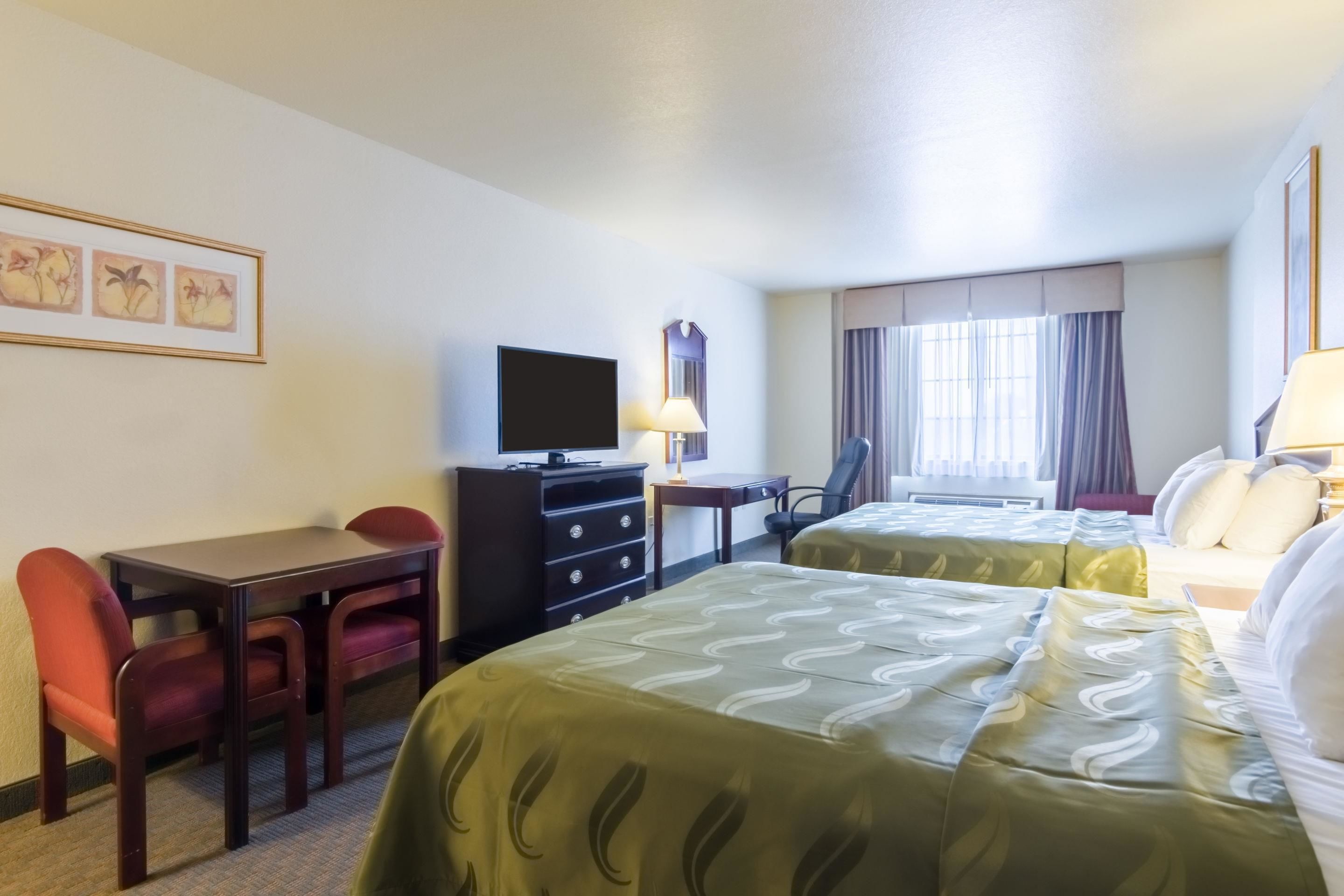 Una habitación de hotel con dos camas, un escritorio con silla, televisión y ventana con cortinas.