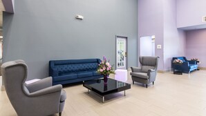 Un vestíbulo moderno con un sofá azul, sillones grises y una mesa de centro negra con un jarrón de flores.