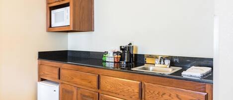 A compact kitchen with wooden cabinets, a built-in microwave, a coffee maker, and a sink.