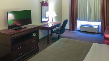 Habitación de hotel con cama, escritorio con silla, televisor, espejo y aire acondicionado.