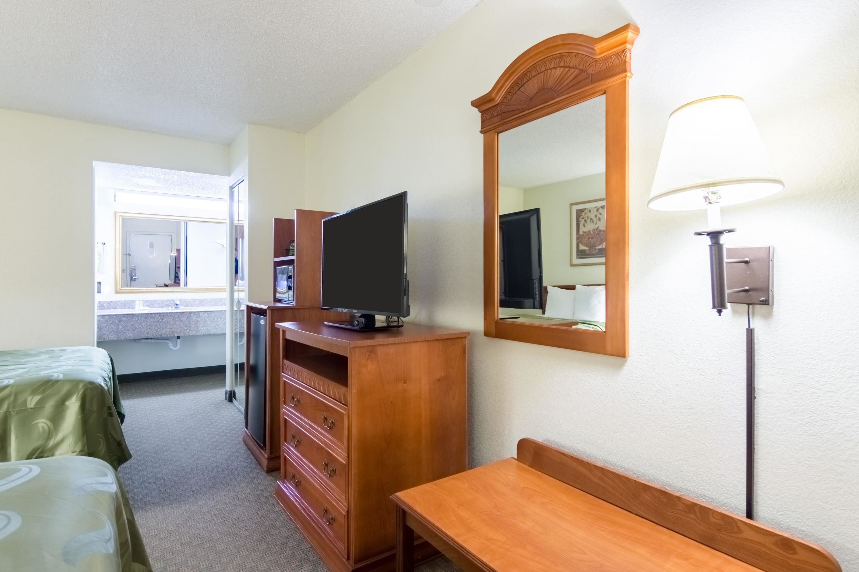 Une chambre d’hôtel avec un lit, une commode en bois, un téléviseur, un miroir et une lampe.