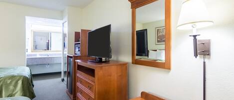 Une chambre d’hôtel avec un lit, une commode en bois, un téléviseur, un miroir et une lampe.