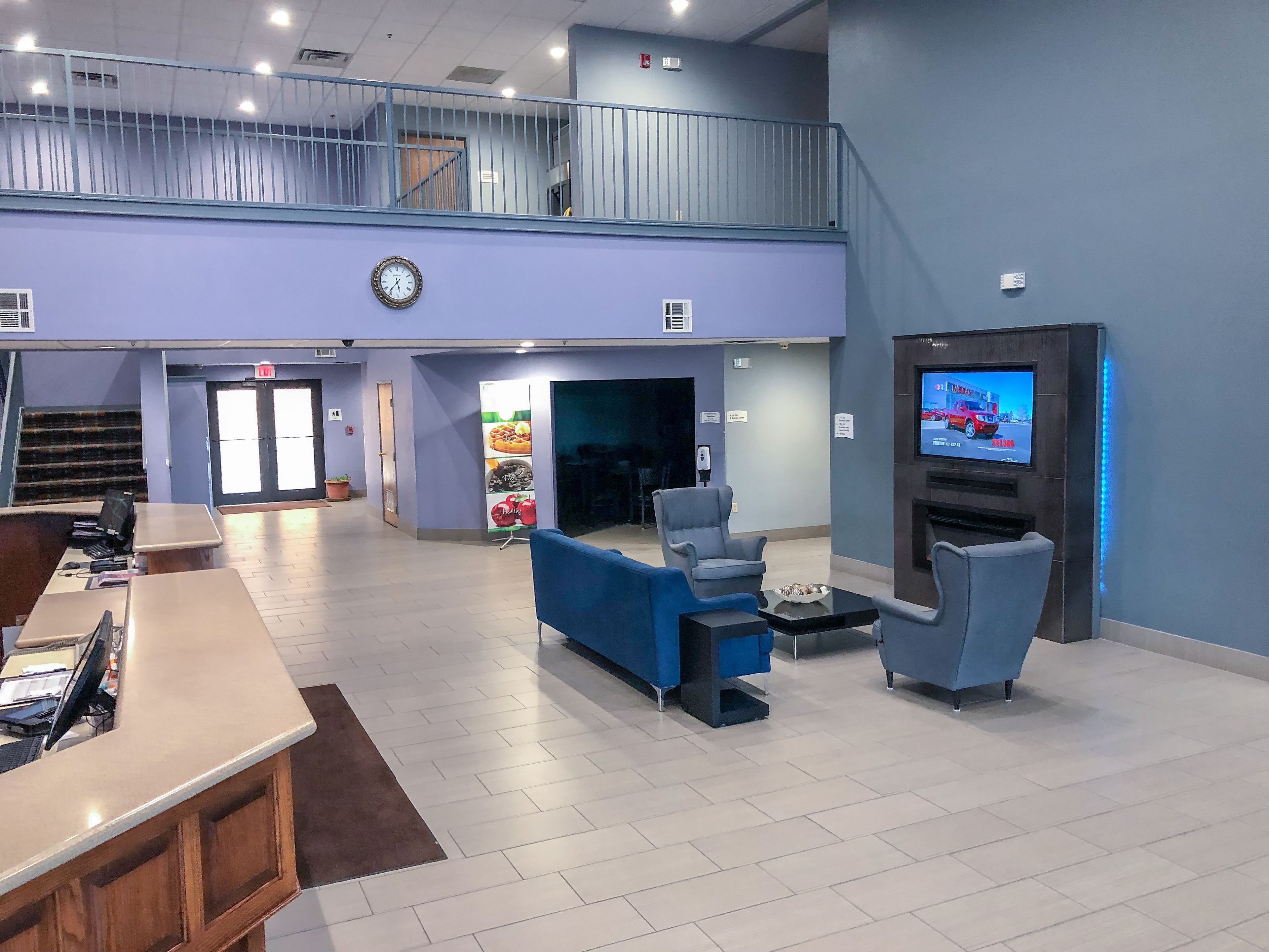 A spacious lobby with a reception desk, seating area, and a television screen.
