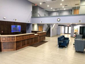 A hotel lobby with a reception desk, a staircase, and seating areas.
