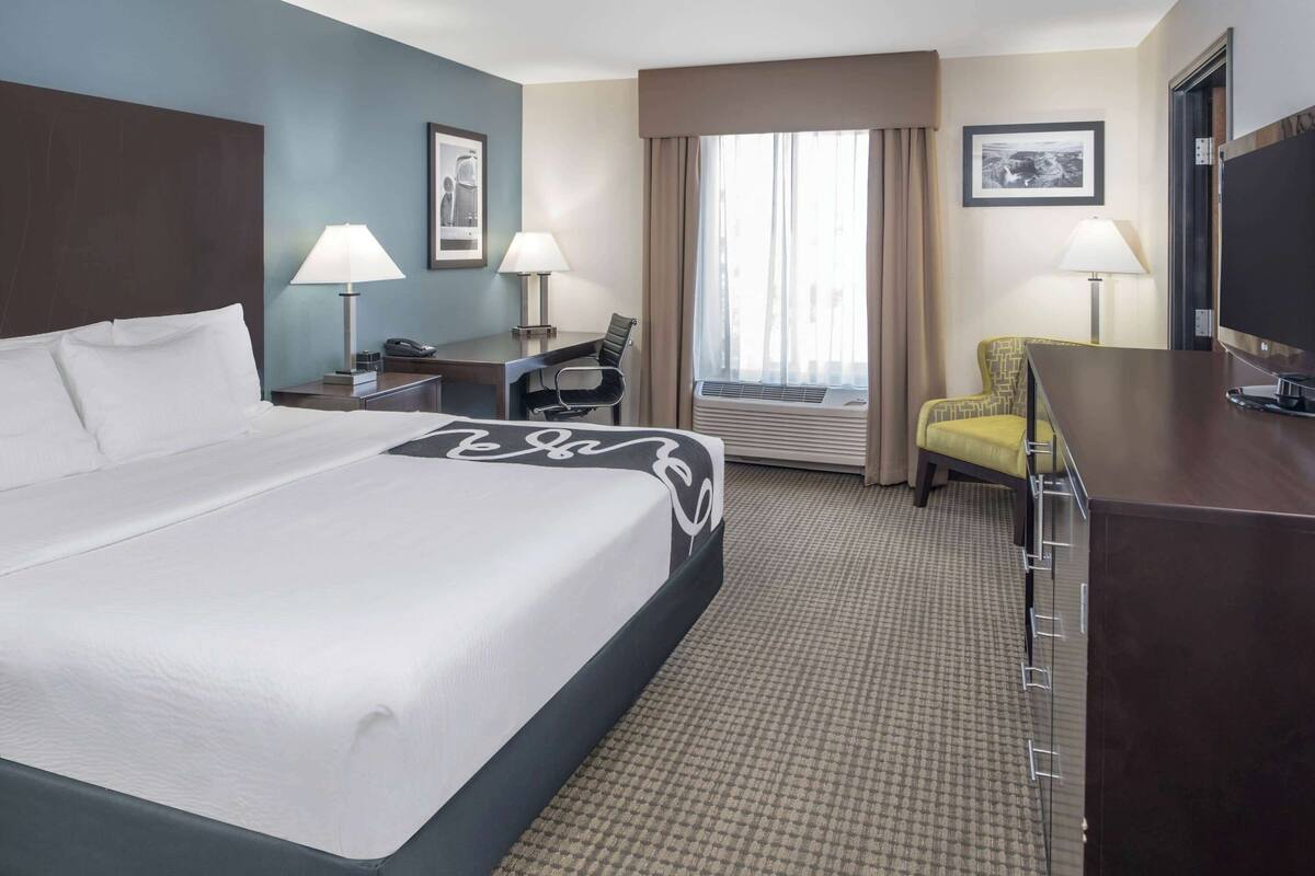A hotel room with a large bed, a desk with a chair, a television, and two lamps.