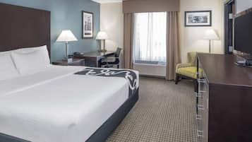 A hotel room with a large bed, two bedside tables with lamps, a desk with a chair, a television, and a window with curtains.